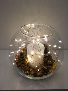 a lit candle in a glass bowl filled with rocks and branches, surrounded by lights