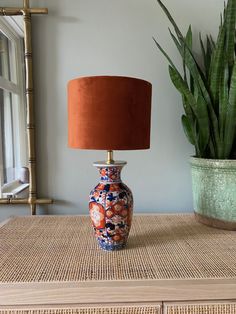 an orange and blue vase sitting on top of a table next to a potted plant