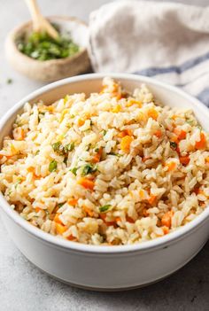 a white bowl filled with rice and carrots next to a wooden spoon on top of a table