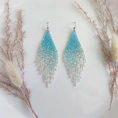 two pairs of blue and white beaded earrings sitting on top of a plate next to dry grass