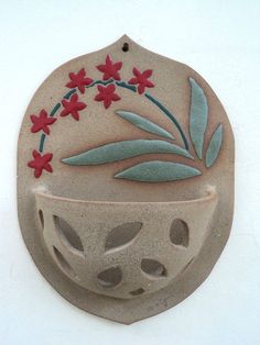 a ceramic vase with red flowers and green leaves painted on it's side, sitting against a white wall