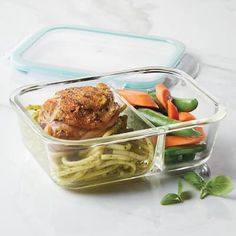 a plastic container filled with food on top of a white counter next to green beans and carrots