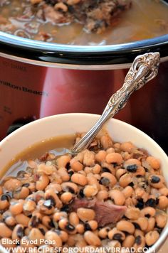 a white bowl filled with beans next to an electric crock pot and a spoon