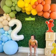 a little boy sitting on a chair in front of a backdrop with balloons and numbers