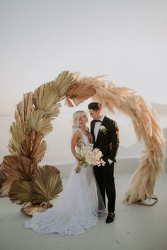 a bride and groom standing under an arch made out of palm leaves