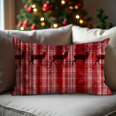 a red plaid pillow sitting on top of a white couch next to a christmas tree