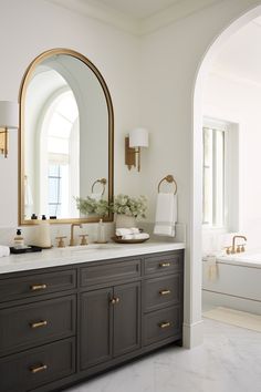 a bathroom with marble counter tops and gold trim on the mirror, along with an arched doorway