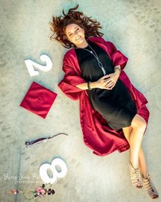 a woman in a graduation gown laying on the ground with her arms around her body