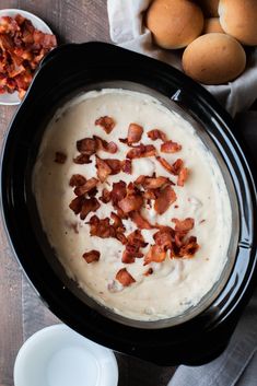 a crock pot filled with cream and bacon next to eggs on a wooden table