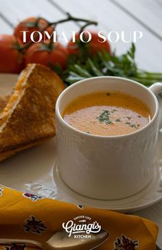 a bowl of soup on a plate next to some bread and tomatoes with the words tomato soup written above it