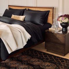 a bed with black sheets and pillows on top of it next to a wooden dresser