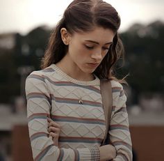 a young woman is looking down at her cell phone while standing outside in the sun