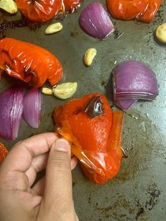 someone is peeling an eggplant into red peppers and onions on a baking sheet