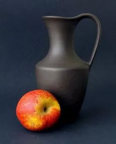 an apple sitting next to a gray vase