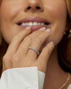 a close up of a person wearing a diamond ring and white shirt with her hand on her chin