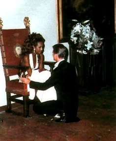 a man kneeling down next to a woman in front of a chair with flowers on it