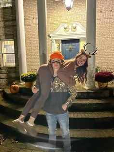 two people posing for a photo in front of a house with deer antlers on their heads