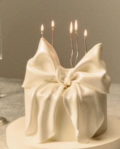 a white cake with three candles on it and a bow around the top that has been made to look like a bow