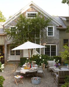 an outdoor patio with chairs, table and umbrella in front of a gray shingled house