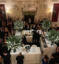 a group of people standing around tables covered in white tablecloths and centerpieces