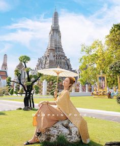 a woman sitting on top of a rock with an umbrella over her head in front of a temple