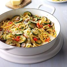 a pan filled with pasta and veggies on top of a table next to cheese