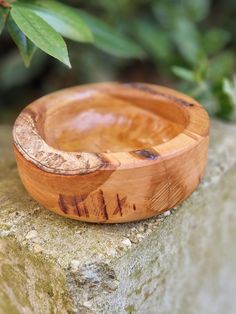 a small wooden bowl sitting on top of a rock next to a green leafy tree