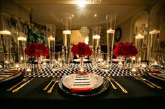 a black and white checkered table cloth with red roses in tall glass vases