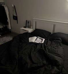 an open book sitting on top of a black comforter covered bed in a bedroom