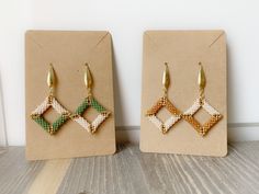 two pairs of earrings are on display in front of a card board with the same design