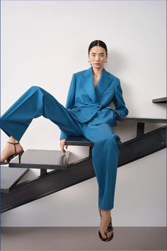 a woman in a blue suit sitting on top of a stair case with her legs crossed