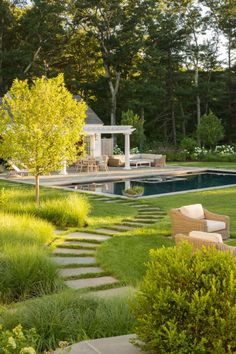 a backyard with a pool, patio and seating area surrounded by trees in the background