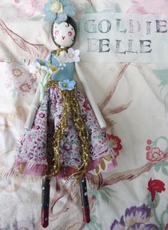 a doll is sitting on top of a bed with floral fabric and gold sequins