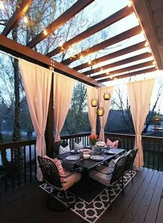 an outdoor dining area on a deck with lights strung over the table and curtains hanging from the ceiling