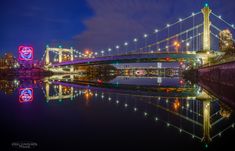 the bridge is lit up at night and reflecting in the water with lights on it