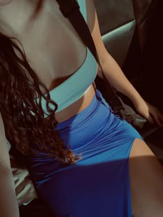 a woman sitting in the back seat of a car wearing a blue top and skirt