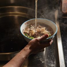 a person is pouring water into a bowl filled with food on top of a stove