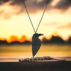 a necklace with a bird on it sitting next to a chain in front of a sunset