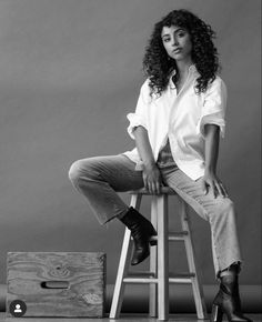 a black and white photo of a woman sitting on a stool