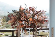 an arrangement of flowers and foliage on a metal fence with mountains in the background at this outdoor wedding venue