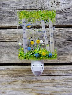 an image of flowers and trees in the woods on a glass night light holder that is attached to a wooden wall