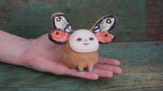 a hand holding a small ceramic animal with two butterflies on it's head and wings