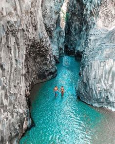 two people are wading through the water in a narrow canyon with blue rocks on either side