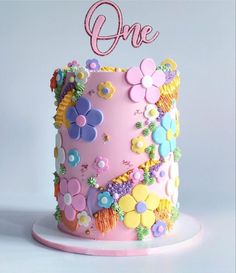 a pink cake decorated with flowers and the word'one'on top is sitting on a plate