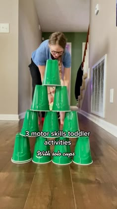 a woman placing green cups on top of each other in the middle of a wooden floor