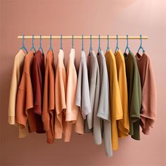 several sweaters hanging on a clothes rack in front of a pink wall with blue hangers