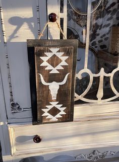 a wooden sign hanging from the side of a white door with a cow skull on it