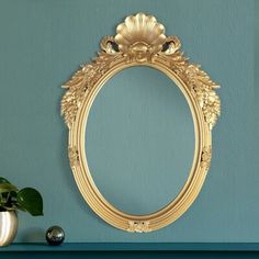 a gold framed mirror on a blue wall next to a potted plant and vase