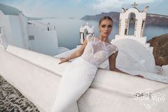 a woman in white dress leaning on the edge of a building with an ocean view