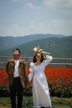 two people standing next to each other with flowers in their hair and one person wearing a white dress